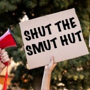 Hand holding a megaphone alongside a hand holding a sign reading "Shut the smut hut"